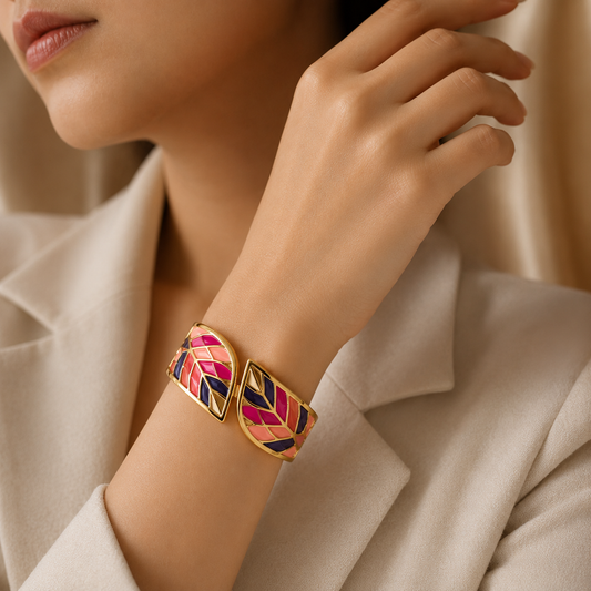 A close-up lifestyle shot of a model wearing a gold-toned cuff bracelet with a colorful chevron pattern in pink, orange, and navy blue.
