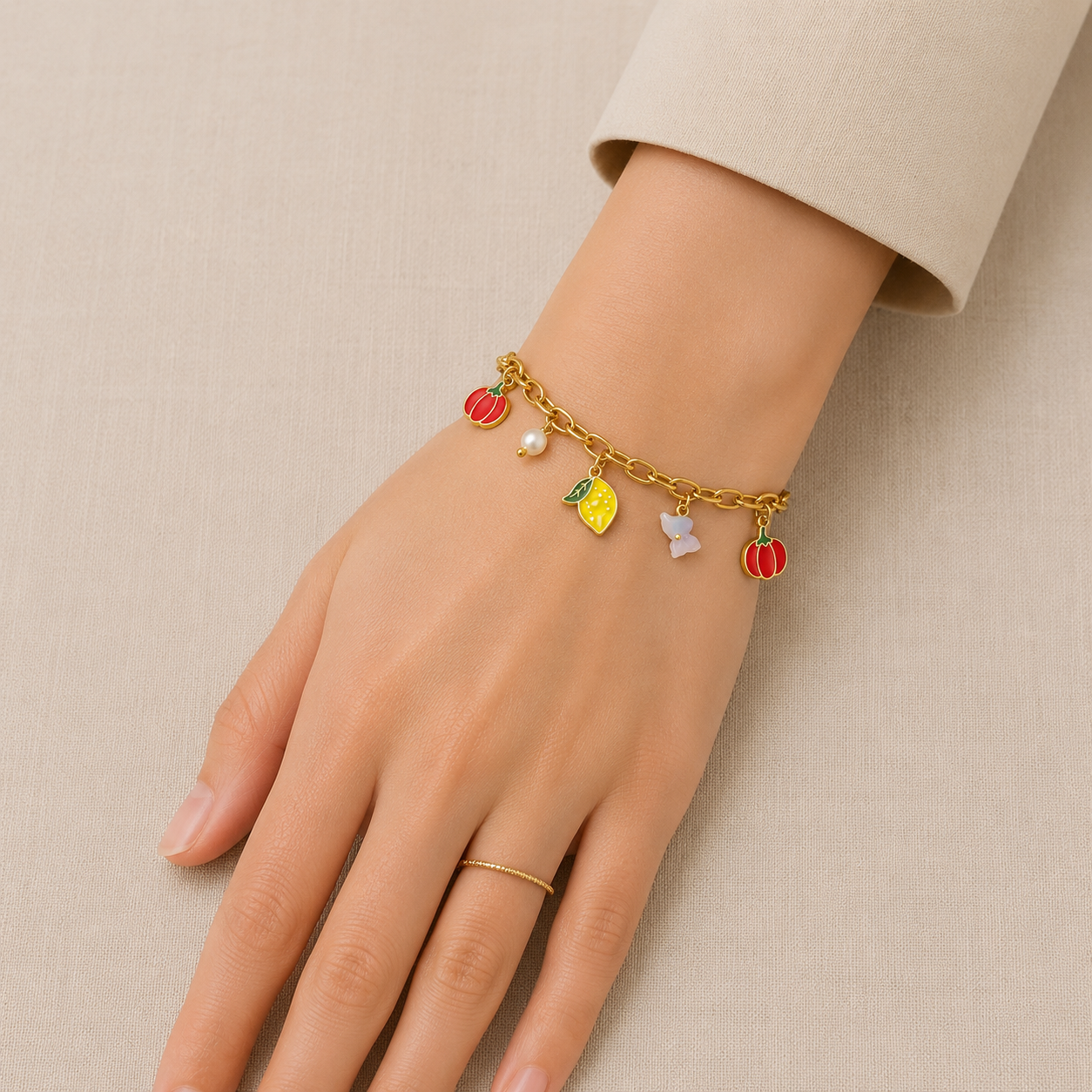 Anti Tarnish charm bracelet featuring pumpkin, lemon, butterfly, and pearl charms worn on a woman's wrist against a cream beige background.