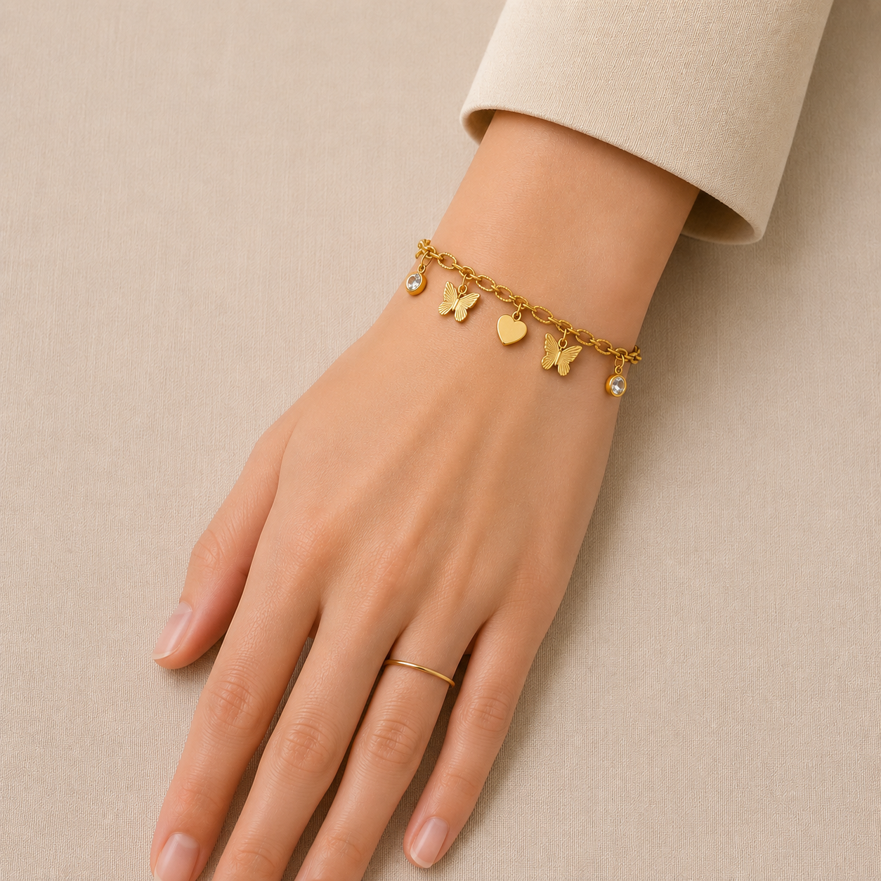 Gold butterfly and heart charm bracelet with crystal accents worn on a woman's wrist against a beige background.