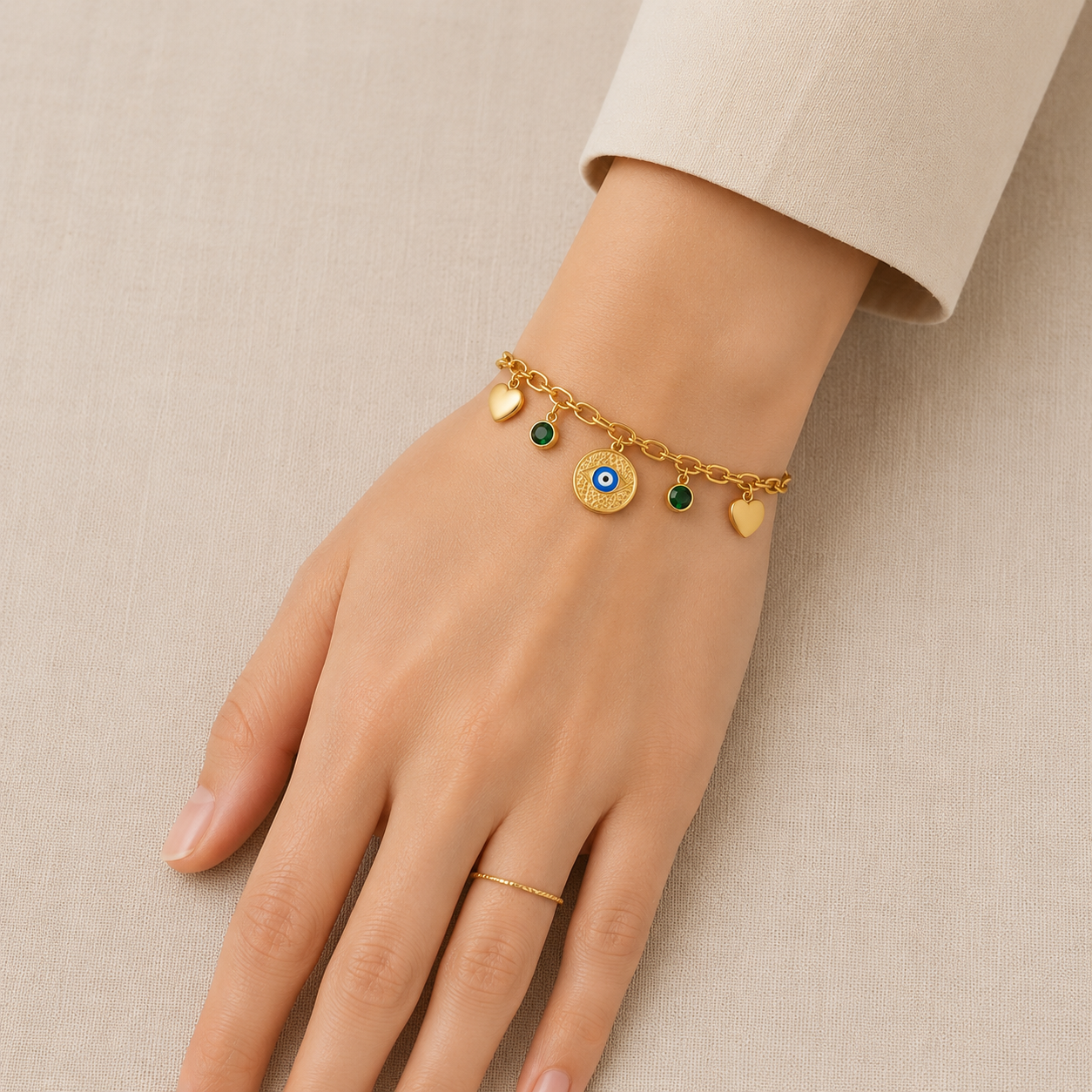 Gold plated Evil Eye charm bracelet with heart charms and green crystal accents for women on beige background.