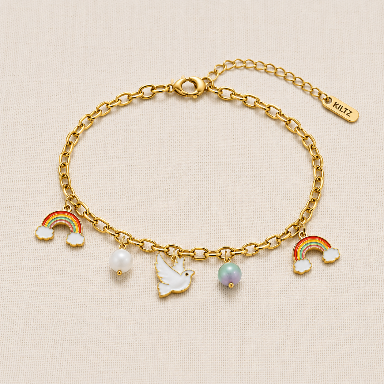 Gold plated rainbow and dove charm bracelet with pearl accents worn on a woman's wrist against a beige background.