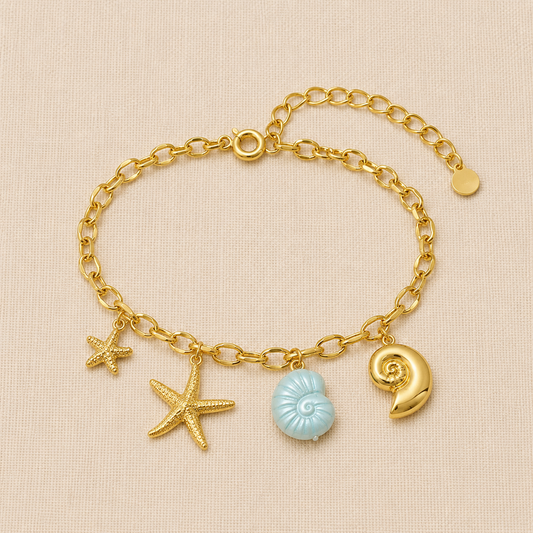 Ocean-inspired gold charm bracelet with starfish and seashell charms on cream linen background.